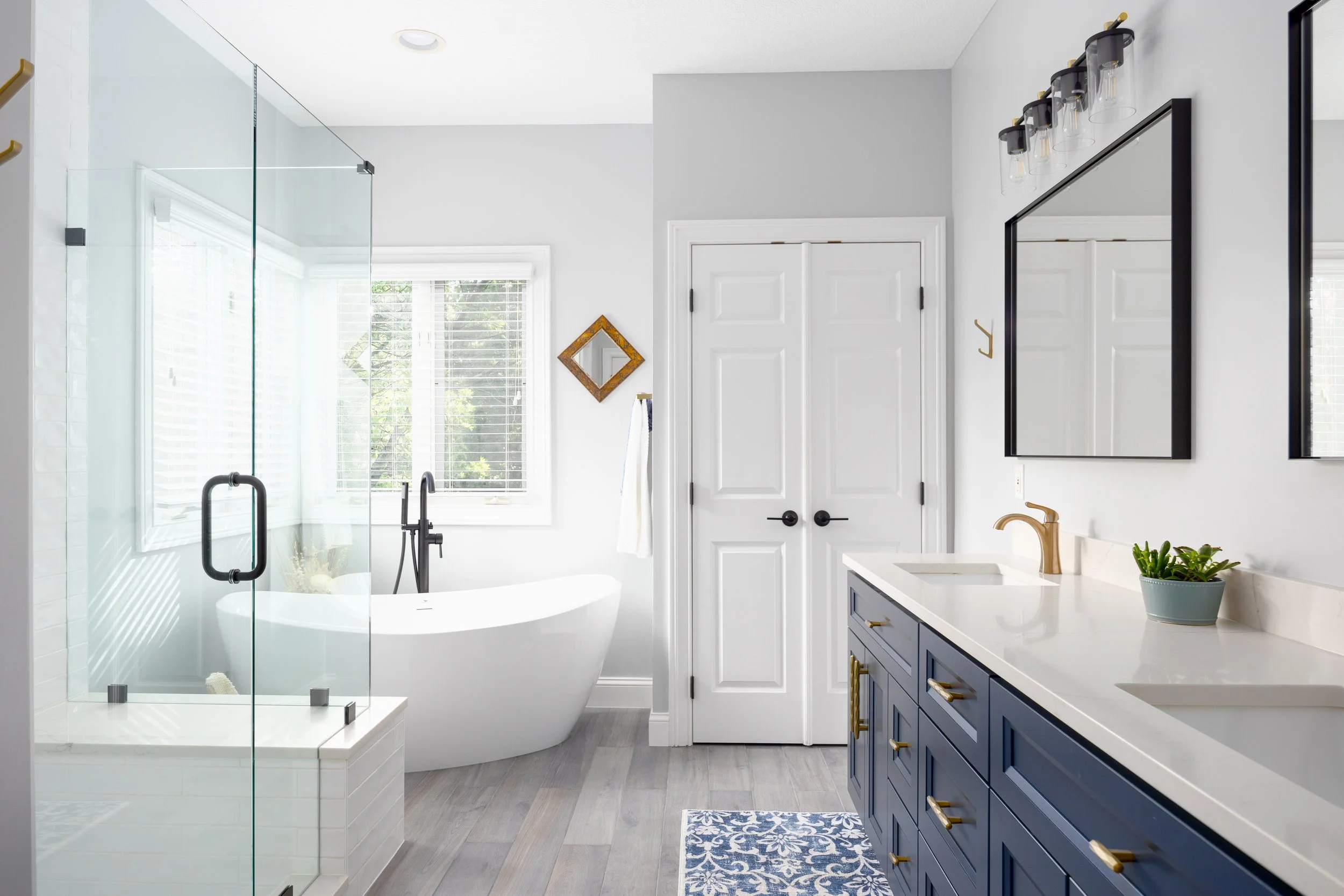Remodeled primary bathroom with navy double vanity, freestanding tub and glass shower
