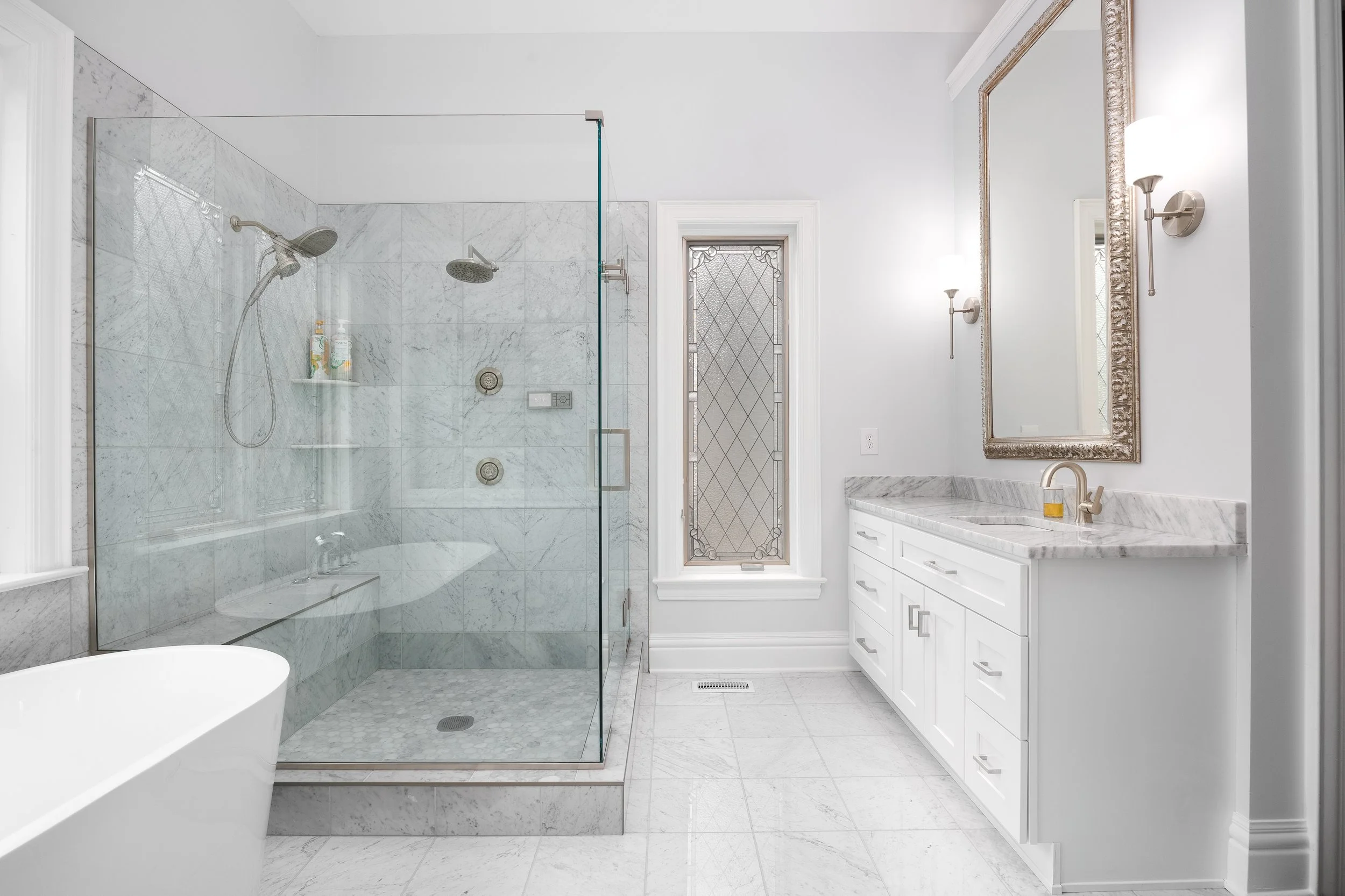 Bathroom with marble tiled corner shower, glass enclosure, bench seat and white shaker vanity